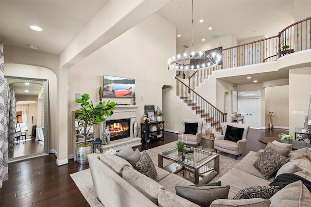 living room featuring stairs, a towering ceiling, a glass covered fireplace, arched walkways, and dark wood finished floors