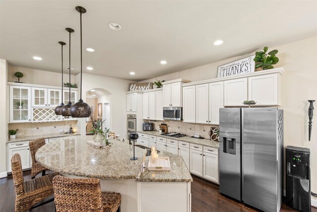 kitchen with backsplash, appliances with stainless steel finishes, arched walkways, white cabinets, and dark wood-style floors