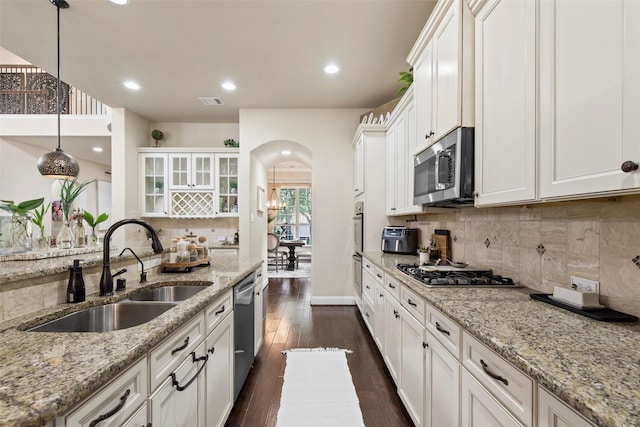 kitchen featuring arched walkways, white cabinets, tasteful backsplash, a sink, and stainless steel appliances
