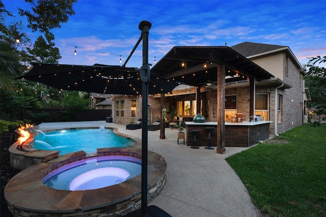pool at dusk with a fenced backyard, outdoor dry bar, a patio area, a pool with connected hot tub, and a yard
