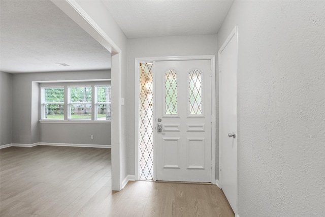 foyer featuring baseboards, a textured wall, and wood finished floors