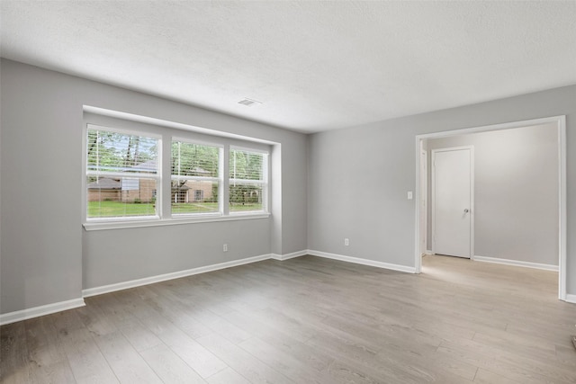 empty room featuring baseboards, visible vents, wood finished floors, and a textured ceiling