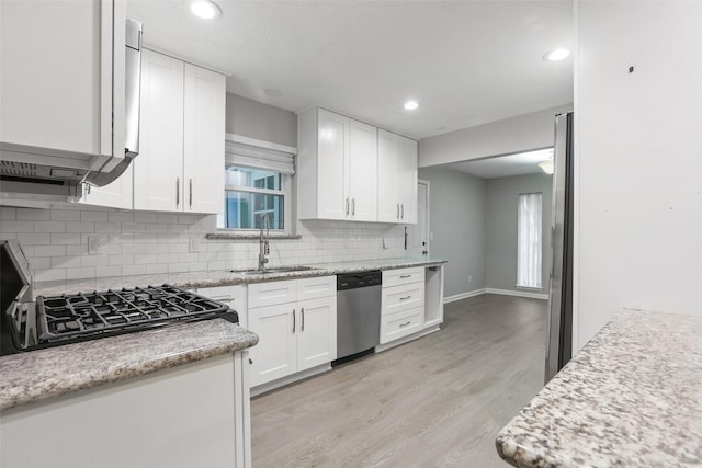kitchen featuring stainless steel dishwasher, a sink, white cabinets, light wood finished floors, and backsplash