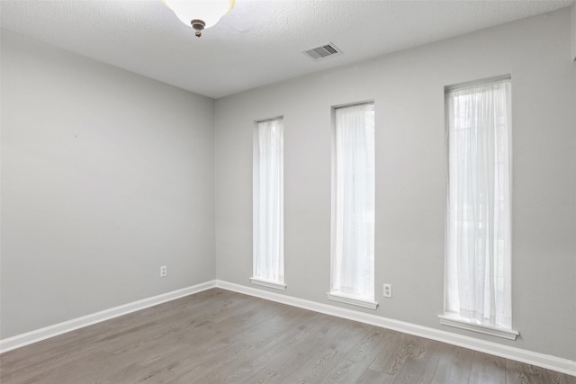 spare room featuring baseboards, wood finished floors, visible vents, and a textured ceiling