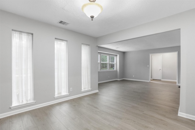empty room with baseboards, wood finished floors, visible vents, and a textured ceiling