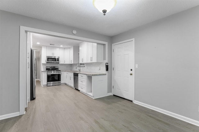 kitchen with white cabinets, a sink, light wood-type flooring, backsplash, and appliances with stainless steel finishes
