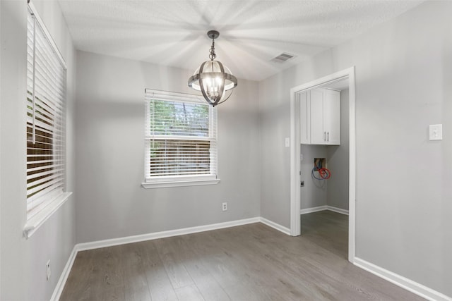unfurnished dining area with a chandelier, wood finished floors, visible vents, and baseboards