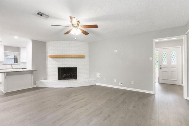 unfurnished living room with baseboards, visible vents, wood finished floors, ceiling fan, and a fireplace