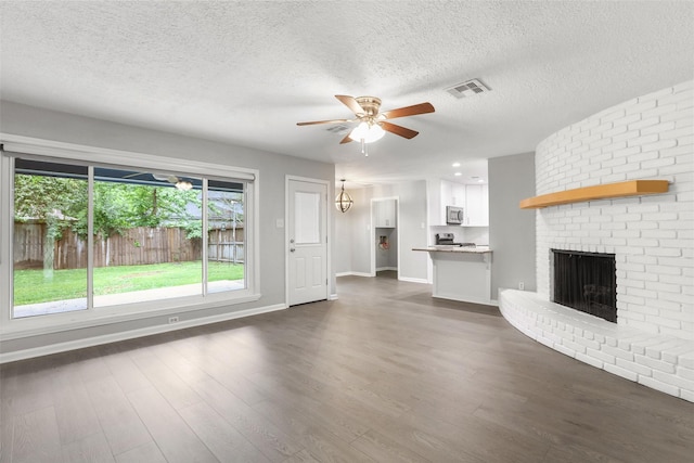 unfurnished living room with a textured ceiling, dark wood finished floors, visible vents, a brick fireplace, and ceiling fan