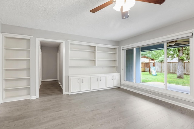 interior space featuring built in shelves, baseboards, a ceiling fan, and light wood-style flooring