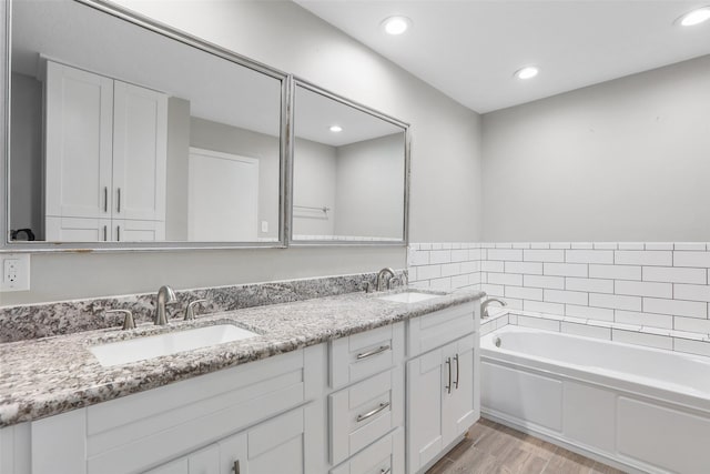full bath with a garden tub, wood finished floors, a sink, and double vanity