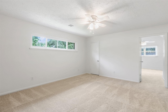 spare room with a textured ceiling, light colored carpet, ceiling fan, and visible vents