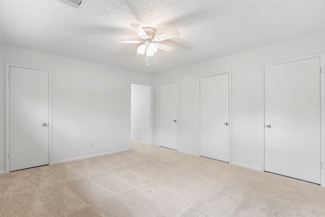 unfurnished bedroom featuring two closets, a textured ceiling, visible vents, and carpet
