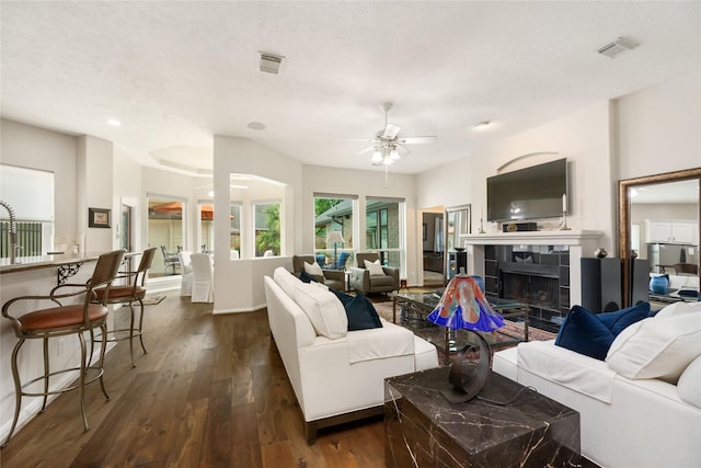 living room with a ceiling fan, visible vents, a tile fireplace, and dark wood-style flooring
