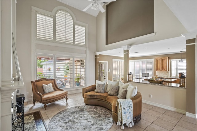 living area featuring a ceiling fan, a high ceiling, light tile patterned flooring, and decorative columns