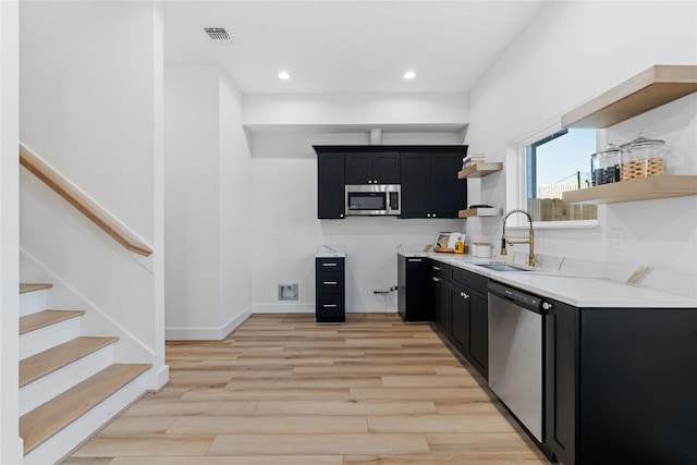 kitchen with stainless steel appliances, a sink, light wood-type flooring, dark cabinetry, and open shelves
