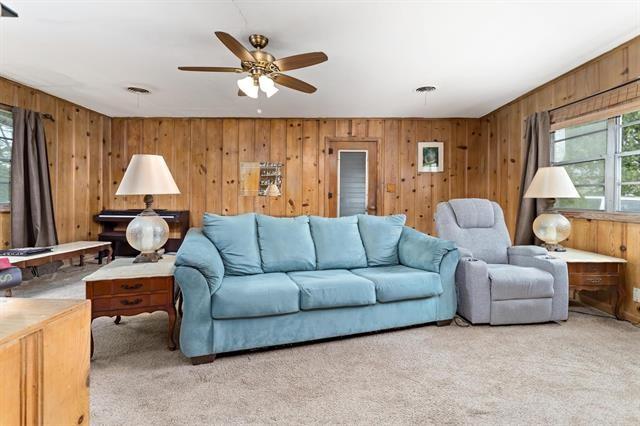 living room with ceiling fan, light carpet, and wood walls