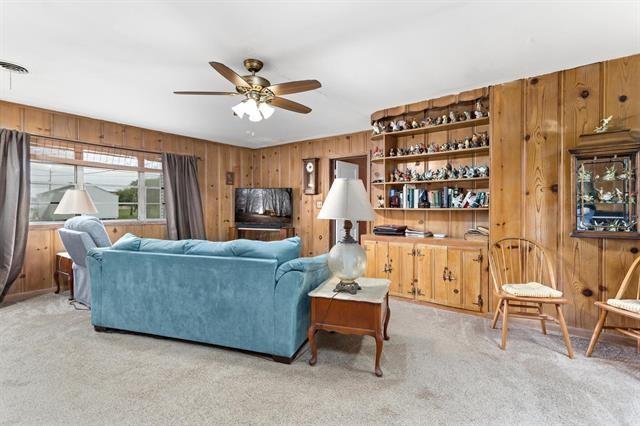 carpeted living area featuring wood walls and ceiling fan