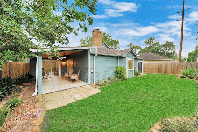 rear view of property with a yard, a chimney, a fenced backyard, and a patio area