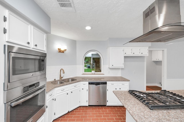 kitchen featuring visible vents, wall chimney range hood, white cabinets, a sink, and stainless steel appliances