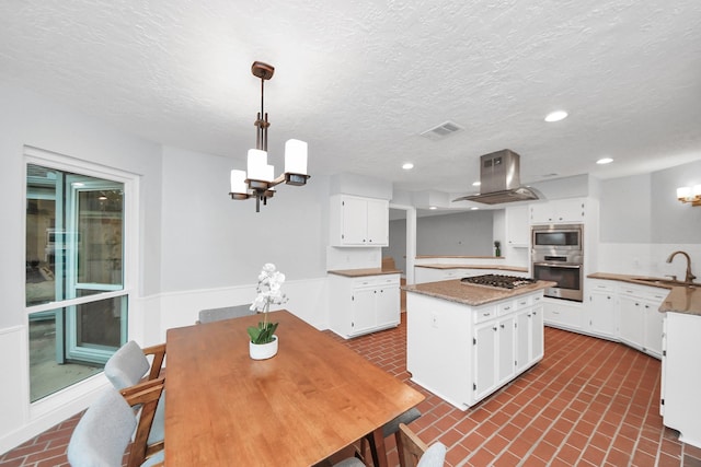 kitchen featuring island range hood, white cabinets, brick patterned floor, a chandelier, and stainless steel appliances