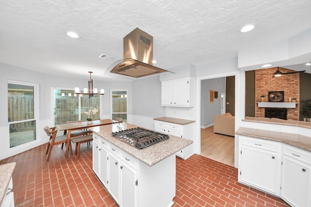 kitchen with island exhaust hood, visible vents, stainless steel gas cooktop, brick patterned floor, and a notable chandelier