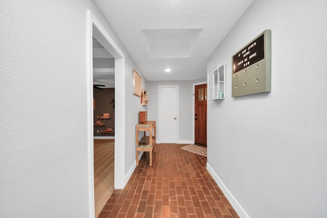 corridor with baseboards, recessed lighting, and brick patterned floor