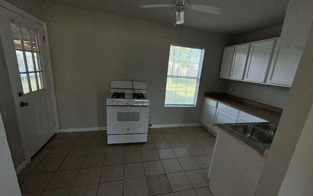 kitchen with white cabinets, light tile patterned flooring, baseboards, a ceiling fan, and white range with gas stovetop
