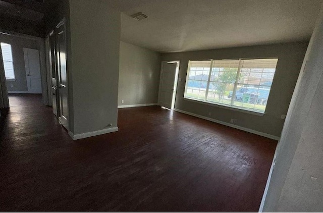 unfurnished room with baseboards, dark wood-type flooring, visible vents, and a wealth of natural light