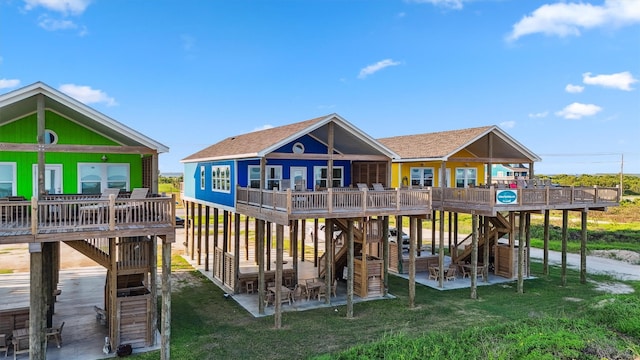 rear view of property featuring a shingled roof, a yard, stairs, and a deck