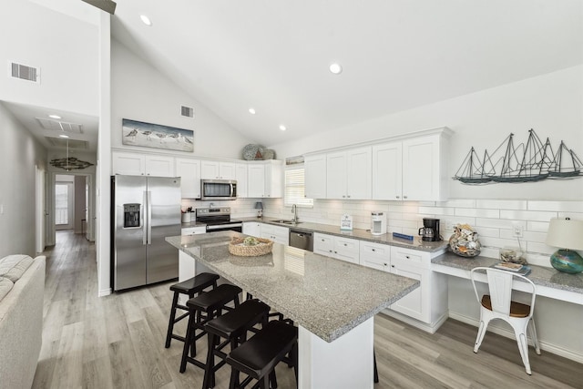 kitchen featuring white cabinets, stainless steel appliances, a sink, visible vents, and a kitchen bar