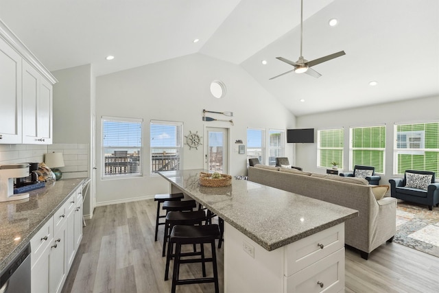 kitchen with light wood finished floors, stone countertops, stainless steel dishwasher, a center island, and a kitchen bar