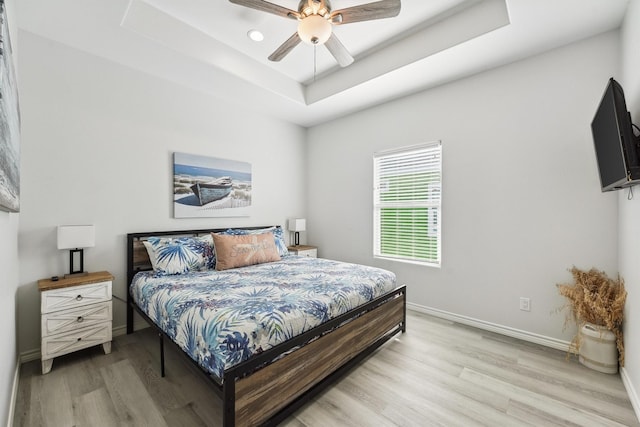 bedroom featuring recessed lighting, a raised ceiling, a ceiling fan, light wood-style floors, and baseboards