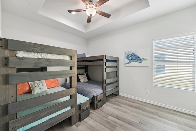 bedroom with a tray ceiling, light wood-type flooring, baseboards, and ceiling fan