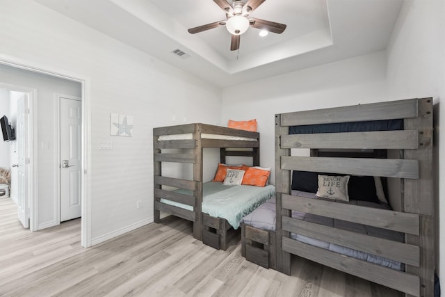 bedroom with a raised ceiling, wood finished floors, visible vents, baseboards, and ceiling fan