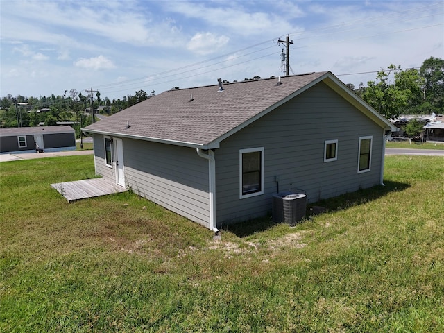 back of house featuring central AC unit, a yard, and a shingled roof