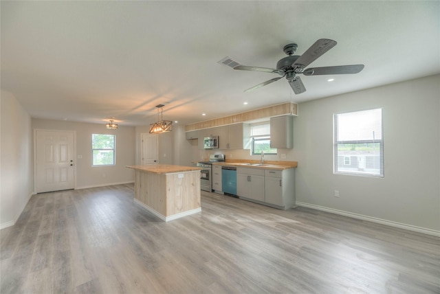 kitchen featuring a sink, stainless steel appliances, light wood-style floors, a kitchen island, and baseboards