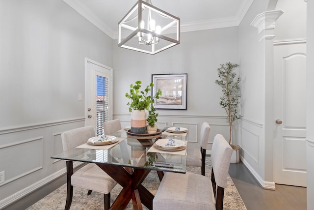 dining space featuring wainscoting, a decorative wall, a chandelier, wood finished floors, and ornamental molding