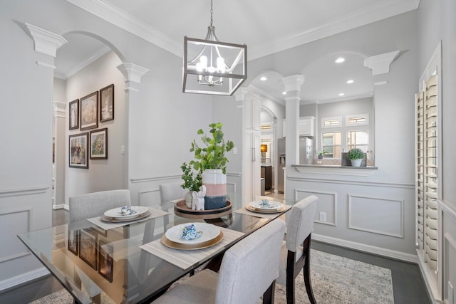 dining area featuring a decorative wall, arched walkways, a wainscoted wall, decorative columns, and ornamental molding