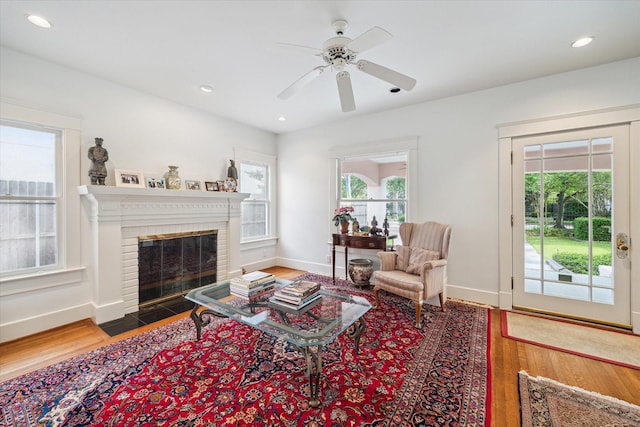 living area with baseboards, recessed lighting, a brick fireplace, wood finished floors, and a ceiling fan