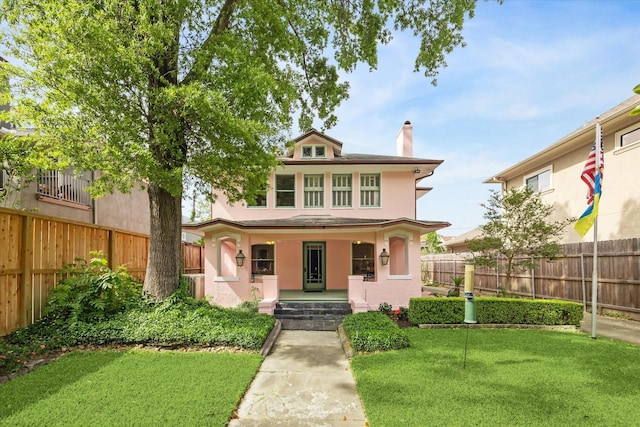 traditional style home with stucco siding, covered porch, a front yard, and a chimney