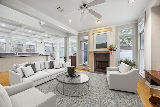 living room featuring a fireplace with flush hearth, beamed ceiling, visible vents, recessed lighting, and light wood finished floors