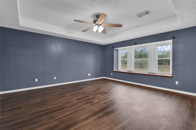 spare room with a ceiling fan, visible vents, dark wood-style floors, and a raised ceiling