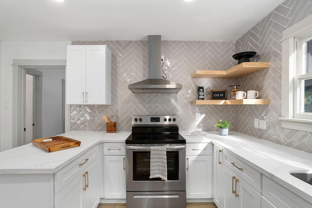 kitchen featuring wall chimney range hood, tasteful backsplash, stainless steel electric stove, a peninsula, and white cabinetry