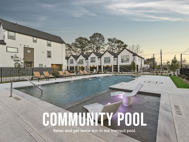 pool at dusk featuring fence, a patio area, a community pool, and a residential view