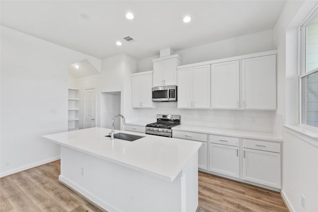 kitchen with white cabinets, stainless steel appliances, a sink, a kitchen island with sink, and tasteful backsplash