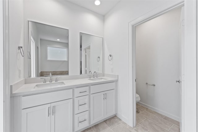 full bathroom featuring recessed lighting, double vanity, toilet, and a sink