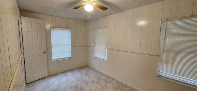 interior space with marble finish floor, wood walls, a ceiling fan, and a textured ceiling