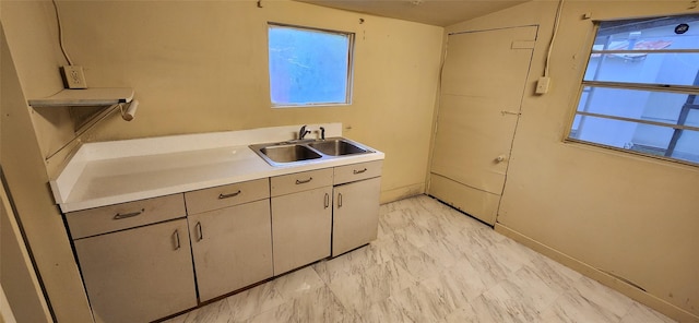 kitchen featuring baseboards, light countertops, gray cabinetry, and a sink
