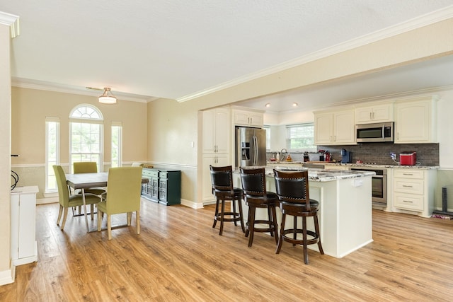 kitchen featuring stainless steel appliances, ornamental molding, a center island, a kitchen bar, and light wood-style flooring